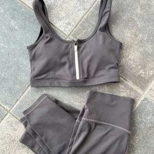 Aim’n set - Snygg grå sporttopp med dragkedja framtill. Perfekt för träning med en stilren design och bekväma axelband, använd enstaka gånger. Tights mer använda. 