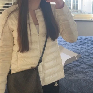 Vit dunjacka med dragkedja - Säljer en stilren vit dunjacka med dragkedja. Jackan har en quiltad design och är perfekt för kyligare dagar. Den är långärmad och har en smidig passform som gör den lätt att bära.