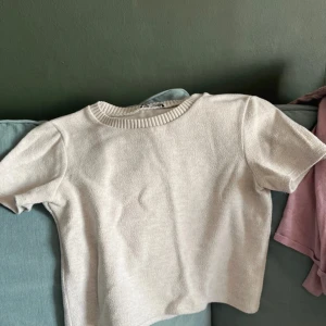 Beige kortärmad topp - Säljer en stilren beige topp med korta ärmar och ribbad halsringning. Perfekt för en enkel och snygg look.