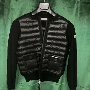 Svart Cardigan från Moncler - Snygg svart jacka från Moncler med quiltad framsida och långa ärmar. Jackan har dragkedja och praktiska fickor framtill. Perfekt för våren och kyligare dagar. Jag är i väldigt fint skick och är använd ett få tal gånger. Priset kan diskuteras ❤️Jacka är Size 2 vilket motsvarar storlek S/M.