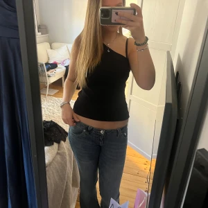 Svart topp - Säljer en stilren svart topp med endast en arm. Perfekt för en enkel och snygg look. Passar bra till både jeans eller kjol.