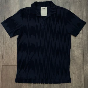OAS Frotté Piké (nyskick) - Snygg mörkblå t-shirt från OAS med ett subtilt mönster. Den har en klassisk krage och korta ärmar, perfekt för en stilren look. Nypris 1200kr!!