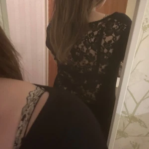 Svart topp med spetsdetaljer - Snygg svart topp med spetsdetaljer på ryggen. Toppen har korta ärmar och en offshoulder-design som ger en elegant look. Perfekt för en kväll ute eller en speciell tillställning.