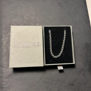 Silverfärgat armband från Lyxery - Snyggt och stilrent silverfärgat armband från Lyxfry. Armbandet har en klassisk kedjedesign och kommer i en elegant förpackning. Perfekt för att ge en touch av elegans till din stil. Nypris 500 