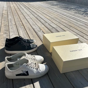 Svarta och vita sneakers från Axel Arigato - Två par stilrena sneakers från Axel Arigato. Ett par i svart med vit sula och ett par i vitt med svart detalj på sidan. Båda paren har snörning och är perfekta för en casual look. Dem svart är i väldigt bra skicka (nästan nya) de vita är bra men lite mer använda. 499 för de svarta (strlk 46) och 299 för de vita strlk (45). Båda paren har box och allt.  Båda för 700.