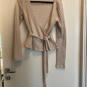 Beige ribbad omlottkofta - Säljer en snygg beige ribbad omlottkofta med knytband i midjan. Koftan har långa ärmar och en v-ringad design som ger en stilren look. Perfekt för lager-på-lager under kyligare dagar. Den är helt ny i storlek XS från Shein 🥰