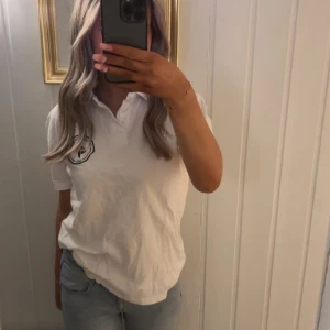 Vit piké från Cross Sportswear - Säljer en klassisk vit pikétröja från Cross Sportswear med broderad logga på bröstet. Tröjan har korta ärmar, krage och knappar framtill. Perfekt för en clean look. (Tycker om dessa jättemycket men har en exakt likadan)