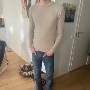 Beige stickad tröja John Henric  - Säljer en stilren beige stickad tröja med rund halsringning. Tröjan har långa ärmar och ribbade muddar vid ärmslut och nederkant. Perfekt för sommar kvällar. Cashmere blandning. Ny pris 2500kr