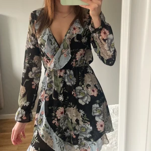 Blommig omlottklänning med volang - Supersöt omlottklänning med blommigt mönster och volangdetaljer. Perfekt för vår och sommar! Storlek S-M