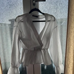 randig omlottblus - Säljer en vit omlottblus med svarta tunna ränder. Blusen har långa ärmar med volang vid ärmslut och midjan är markerad med resår. Perfekt för en trendig och stilren look. Står tyvärr ingen storlek men passar mig som vanligtvis har s❣️pris kan diskuteras !!!