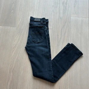 Svarta skinny jeans från Nudie Jeans - Säljer ett par svarta skinny jeans från Nudie Jeans med klassisk femficksdesign och diskret logga på bakfickan. Jeansen har normal passning i midjan och är tillverkade i stretchig denim för en bekväm känsla. Fråga om du har några funderingar 🤩