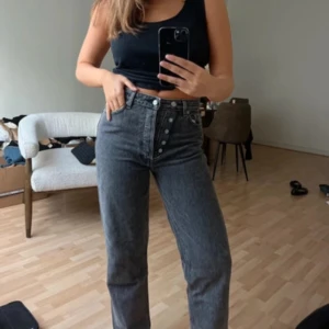 Grå jeansbyxor från Ganni - Säljer ett par grå jeansbyxor från Ganni med raka ben och hög midja. Byxorna har knappar framtill och klassisk femficksdesign. Perfekta för dig som gillar en stilren och tidlös look.