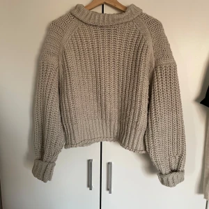 Beige stickad tröja från H&M - Säljer en chunky beige stickad tröja från H&M med bred krage och långa ärmar. Tröjan har en oversized passform och grovstickad struktur.