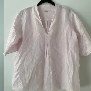 Ljusrosa linneskjorta från Stenströms - Säljer en stilren ljusrosa skjorta från Stenströms i linne. Skjortan har en v-ringad design och korta ärmar, perfekt för en avslappnad look. Den är tillverkad i ett luftigt material som passar bra för varmare dagar.