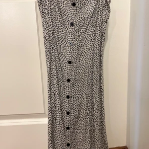Mönstrad klänning från Divided - Snygg klänning från Divided med svart blommönster på vit bakgrund. Klänningen har knappar framtill och smala axelband. Passar XS