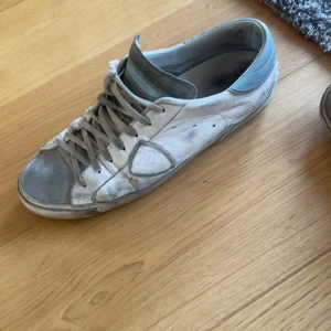 Vita sneakers från Philippe Model med grå detaljer - Säljer ett par vita Philippe Model sneakers med grå detaljer och ljusblå häl. Skorna har snörning och en platt sula. Klassisk design med rund tå och diskret logga på sidan. Perfekta för dig som gillar stilrena sneakers. Storlek 43 
