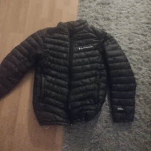 Svart dunjacka från Peak Performance - Säljer en svart dunjacka från Peak Performance. Jackan har lång ärm, dragkedja framtill och klassisk pufferdesign. Perfekt för kyligare dagar och enkel att matcha med olika outfits.