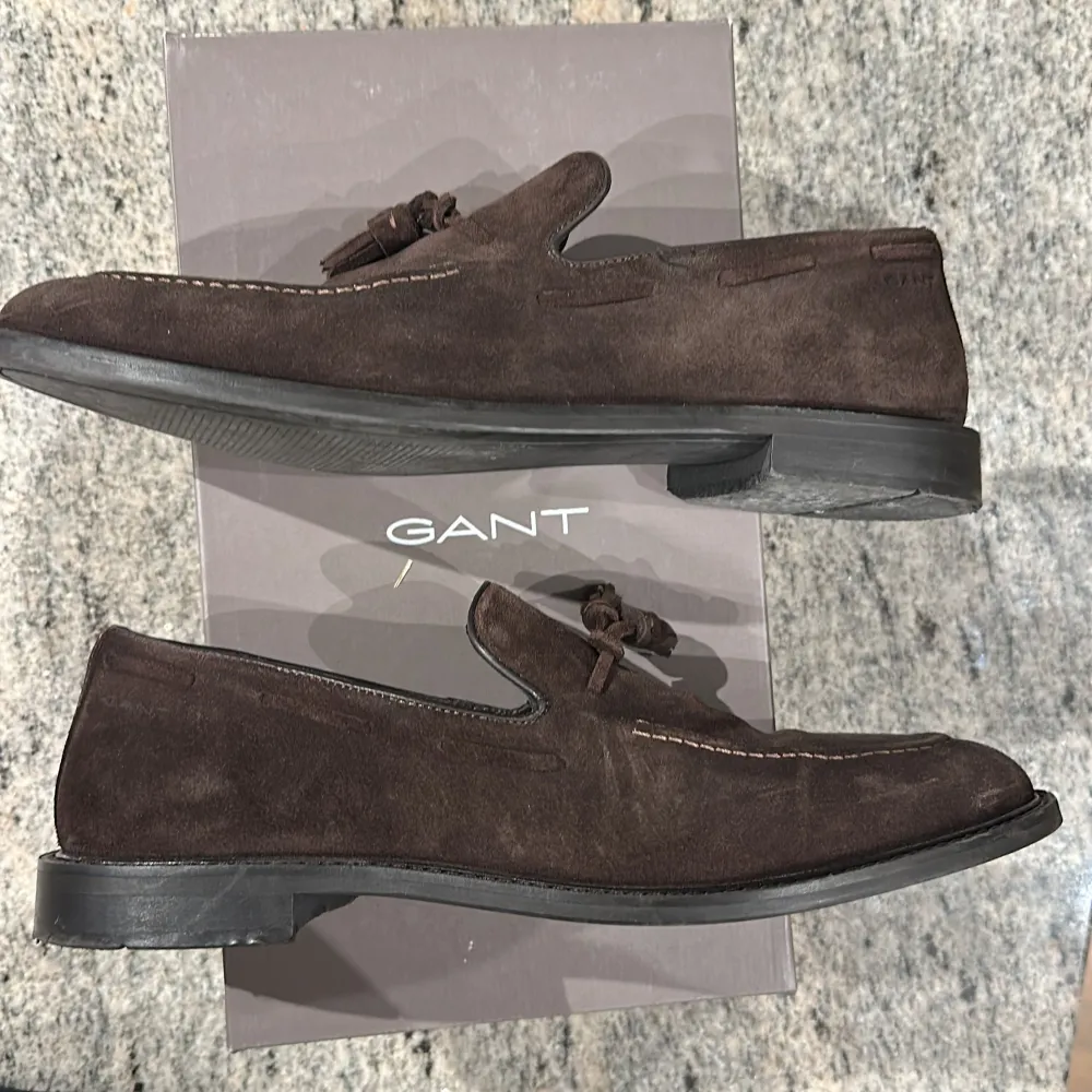 Säljer ett par stilrena bruna loafers i mocka från GANT. Skorna har dekorativa tofsar framtill, rund tå och diskreta sömmar längs ovandelen. Perfekta för dig som gillar klassisk och tidlös stil.. Kengät.