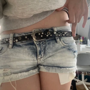 Svart bälte med nitar - Snyggt svart bälte dekorerat med silverfärgade nitar och ringar. Perfekt för att ge en edgy touch till din outfit. Bältet har en klassisk spänne och passar bra till jeans eller shorts.