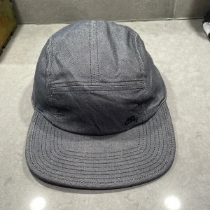 Grå keps från Nike SB - Snygg grå keps från Nike SB med justerbart spänne baktill. Kepsen har en stilren design med diskret logga på framsidan. Perfekt för en avslappnad stil.