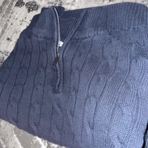 Mörkblå stickad tröja med dragkedja - Säljer en mörkblå stickad tröja med halv dragkedja och kabelstickat mönster. Tröjan har hög krage och långa ärmar, perfekt för kyligare dagar. Snygg och enkel att matcha till olika outfits.