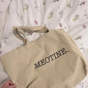Tygväska Meotine - Säljer en beige Tygväska från Meotine med svart tryck. Perfekt storlek för att bära med sig allt man behöver till skolan eller stan och varför inte stranden? Väskan har två långa handtag och två kortare. Den är enkel att matcha med olika outfits. Aldrig använd. (Nypris 999kr) pris går att diskutera.