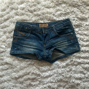 Lågmidjade shorts - Snygga blå jeansshorts med klassisk femficksdesign och slitna detaljer framtill. Shortsen har låg midja och korta ben, perfekta för varma dagar. Bakfickorna har dekorativa sömmar i orange. Enkelt att matcha med allt.