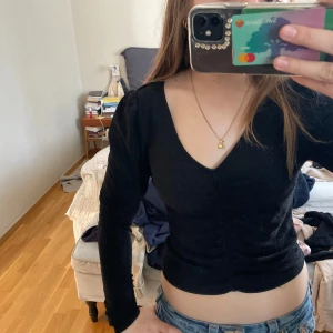 Svart glittrig topp från Monki - Säljer en svart glittrig topp från Monki med v-ringning och långa ärmar. Toppen har en åtsittande passform och rynkdetaljer framtill. Perfekt för en kväll ute eller en festlig tillställning. ✨