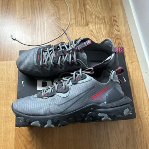 Nya Nike React (Nypris 1,750kr) - Stilrena & Sportiga. Säljer ett par grå Nike React med röda detaljer, riktigt snygga och bekväma. De har en unik vågig sula, klassisk snörning och en diskret Nike-logga på sidan. Perfekta för dig som vill ha en stilren sneaker med sportig känsla. Använda endast ett par gånger – i princip som nya. Du hittar inte bättre pris för detta skick. Först till kvarn! (Passar 42 och 43) strlk 42,5