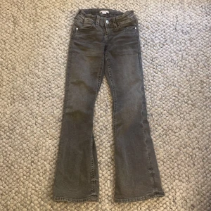 Grå jeansbyxor från Gina Tricot - Snygga grå jeansbyxor från Gina Tricot i storlek 152. Byxorna har raka ben med lätt utsvängd bootcut-stil och dekorativa bakfickor med flätad detalj. Klassisk femficksmodell med knapp och dragkedja framtill.