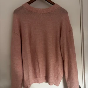 Rosa stickad tröja - Mysig rosa stickad tröja med rund halsringning och långa ärmar. Tröjan har en avslappnad passform och ribbade muddar vid ärmslut och nederkant. Perfekt för lager-på-lager under kyliga dagar.