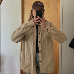 Beige overshirt  - Säljer en beige overshirt med svarta knappar och två bröstfickor. Skjortan har lång ärm och är tillverkad i ett kraftigare material. Perfekt att bära som en oversized skjorta eller som en tunn jacka!