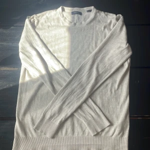 Ljusgrå/beige tunn stickad tröja från Jack&Jones - En stilren ljusgrå/ beige stickad tröja från Jack&Jones. Tröjan har rund halsringning, långa ärmar och breda ribbade muddar vid ärmslut och nederkant. Perfekt för lager-på-lager och enkel att matcha.