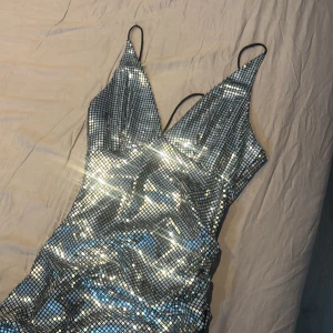 Glittrig silver långklänning med smala axelband - Säljer en maxad glittrig långklänning i silver med smala axelband och v-ringning. Klänningen har en figurnära passform och är täckt av små paljetter som ger en riktig wow-effekt. Perfekt för dig som vill sticka ut på festen! Den är helt ny och aldrig använt!