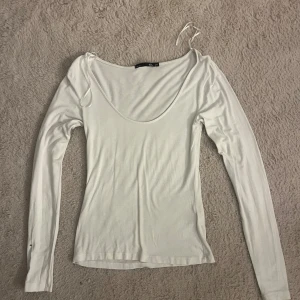 Vit långärmad topp med djup urringning - Säljer en vit långärmad topp. Toppen är figurnära och har en enkel, stilren design som passar till många olika outfits.