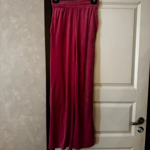 Rosa mjukisbyxor med vida ben - Säljer ett par rosa mjukisbyxor med resår i midjan. Byxorna är i ett mjukt och skönt velour material, perfekta för en avslappnad stil. Passar dig som gillar bekväma och trendiga plagg.