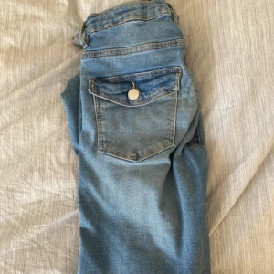 Blå jeans från Gina Tricot - Snygga blå jeansbyxor från Gina Tricot i klassisk modell med fem fickor och knappstängning. Byxorna har en rak passform och är tillverkade i mjukt denimtyg. Perfekta för en avslappnad stil.