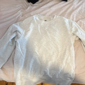 Ljusgrå sweatshirt från Uniqlo - Säljer en stilren ljusgrå sweatshirt från Uniqlo i storlek M. Tröjan har rund halsringning och ribbade muddar vid ärmslut och nederkant. Perfekt basplagg för garderoben!