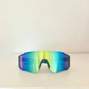 Sportiga solglasögon  - Säljer ett par sportiga solglasögon med stora, blå och gröna spegelglas och svart båge. Perfekta för träning utomhus och ger en futuristisk look🤵🏼 Lätta och bekväma att bära under långa pass😎