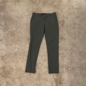 Grå kostymbyxor med normal passform - Snygga grå kostymbyxor med klassisk rak passform och diskreta fickor i sidorna. Byxorna har midwaist och stängs med knapp och dragkedja. Perfekta till en stilren look.