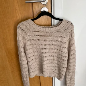 Beige stickad croppad tröja från Hollister, stl XS - Säljer en beige stickad croppad tröja från Hollister. Tröjan har ett luftigt hålmönster, lång ärm och v-ringning. Perfekt för lager-på-lager och ger en avslappnad men trendig look.