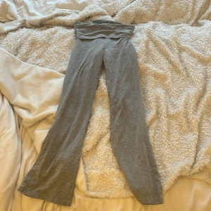 Grå mjukisbyxor från Gina Tricot - Grå joga mats från Gina Tricot med bred, vikt midja och utsvängda ben. Perfekta för en avslappnad stil och superbekväma att ha på sig. Mjukt material som känns skönt mot huden. Andvända knappt råkade beställa fel storlek och hade redan dragit av lappen