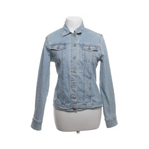 Ljusblå jeansjacka  - Säljer en ljusblå jeansjacka med klassisk krage och knäppning framtill. Jackan har två bröstfickor med lock och knappar samt långa ärmar. Tillverkad i bomull med lite stretch för extra komfort.