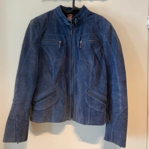 SAKI läder jacka / Blå mockajacka med dragkedjor  - Snygg blå mockajacka med fyra dragkedjefickor framtill och markerade sömmar. Jackan har lång ärm med dragkedja vid ärmslut och quiltad detalj baktill. Figurnära passform och hög krage. Strl 40 men passar S/M bra