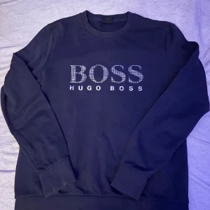 Mörkblå sweatshirt från Hugo Boss - Säljer en mörkblå sweatshirt från Hugo Boss med BOSS-logga i vitt framtill. Tröjan har rund halsringning och långa ärmar. Perfekt för en stilren och avslappnad look. Passar S och M bara att höra av sig vid minsta tanke! Pris kan diskuteras även här😊😊