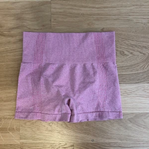Ljusrosa seamless träningsshorts - Säljer ett par ljusrosa seamless träningsshorts ribbad linning. Shortsen har diskreta håldetaljer längs sidorna och är stretchiga för extra komfort. Perfekta för gymmet eller yoga.