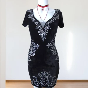 Gotisk Sammetklänning med Strass – Whimsy Goth / Y2K Glam / Mörk Feststil – Soky & Soka -        Märke: Soky & Soka     • Storlek: S / 36 / UK 8     • Skick: Ny utan prislapp, aldrig använd     • Material: Mjuk stretchig sammet med     strass     • Färg: Djupsvart med silverdetaljer     • Passform: Bodycon, mini-längd Stiltips:     • Styla med kängor och svart choker för en whimsy goth-look     • Matcha med höga klackar och silveraccessoarer för en Y2K-festoutfit     