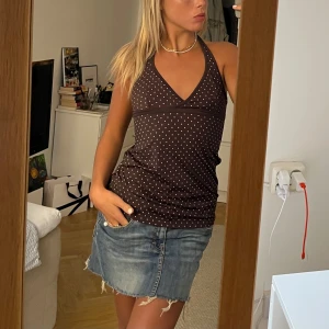 Brun prickig halterneck-linnetopp - Säljer en brun halterneck-linnetopp med rosa prickar och djup v-ringning. Toppen knyts i nacken och har en figurnära passform. 