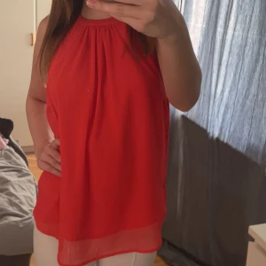 Orange/röd ärmlös blus med halterneck - Säljer en röd/orange, luftig blus med halterneck och öppen rygg. Materialet känns lätt och svalt mot huden.