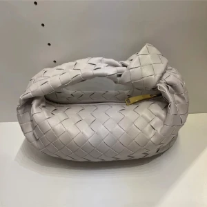 Vit/grå bottega liknande väska  - Säljer en snygg vit/grå axelväska med flätad design likande bottega. Väskan har en kort axelrem och stängs med dragkedja i guld. Perfekt för att lyfta din outfit med en trendig accessoar.